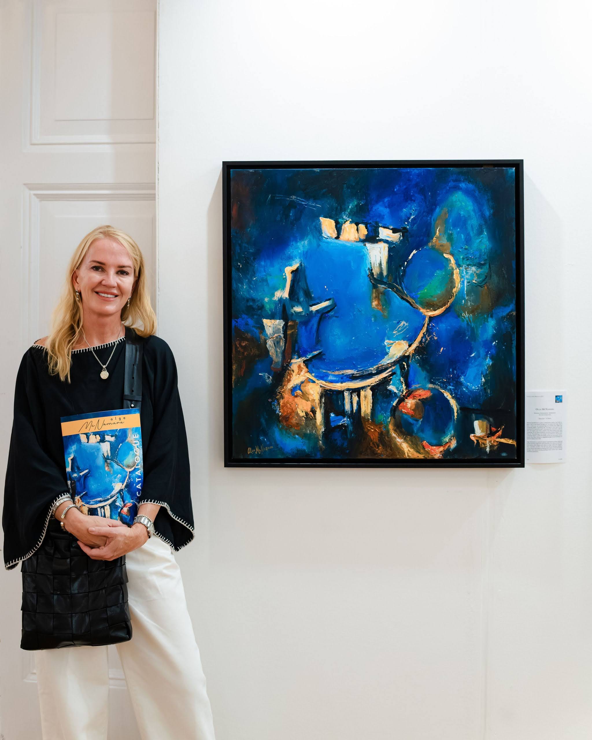 An exhibiting artist standing beside her painting at the Biennale, the catalogue in her hands.