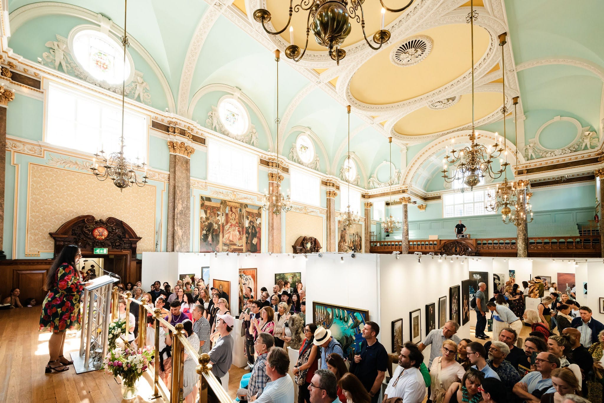 The awards ceremony seen from the balcony: a crowd filling the main hall beneath gilded plasterwork and chandeliers.