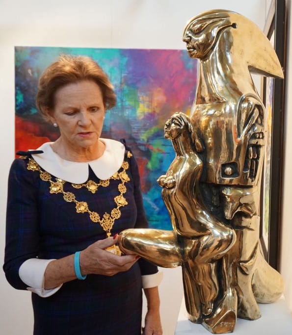 The Mayor of Kensington and Chelsea, in her chain of office, looking at a gilded sculpture.